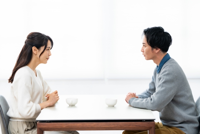 一対一の商談シーン、男女のビジネスパーソンが向かい合い、一方が質問リストを見ながら話している、会議室かカフェ