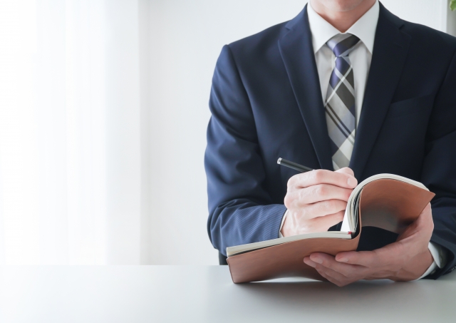 手帳の前で悩んでいる一人社長の後ろ姿
