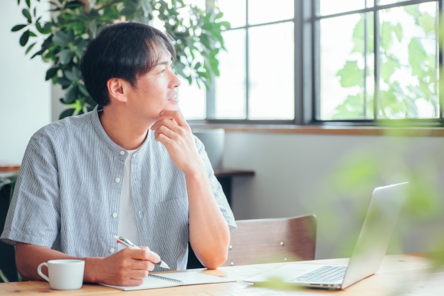 カフェで手帳にメモを書きながら一人で考えている男性ビジネスパーソン
